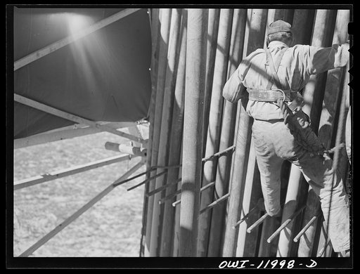 Untitled photo, possibly related to: Andrews County, Texas. Derrick man putting pulled drill pipe in place. He is 120 feet above the ground