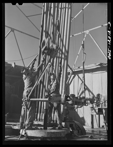 Amdrews County, Texas. Roughnecks reaching for descending traveling block during pipe pulling operations