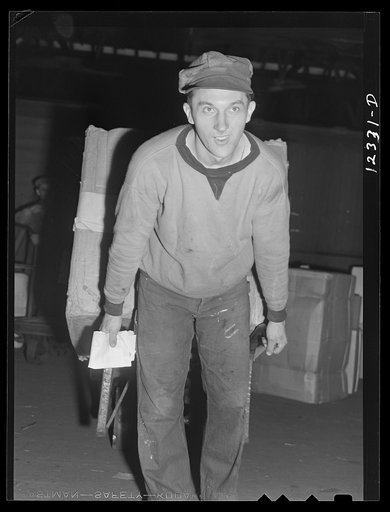 Cihcago, Illinois. Workman in the freight house at the Chicago and Northwestern Railroad yards, pulling a hand truck