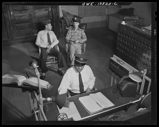 Washington, D.C. Firehouse Station No. 4. Lieutenant Mills on duty at the alarm desk. Two probation firemen in the rear quiz each other on the quarterly examinations they must take during their probation period