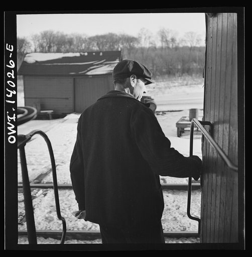 Freight train operations on the Chicago and Northwestern Railroad between Chicago and Clinton, Iowa. The conductor standing on the caboose platform ready to hop off as the train passes the yard office at the end of the trip