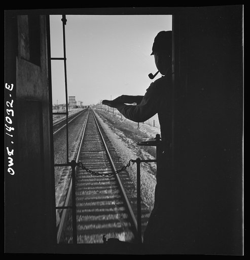 Untitled photo, possibly related to: Freight train operations on the Chicago and Northwestern Railroad between Chicago and Clinton, Iowa. As the train goes through a small town, the conductor exchanges high signs with a switch tender