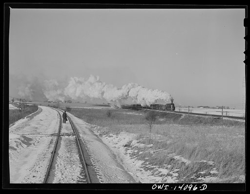 Brakeman standing with a flag, waiting for a Chicago and Northwestern Railroad fast passenger train to go by so that his train can get on the main line in Illinois