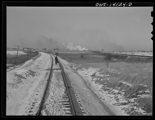 Rear brakeman standing with a flag behind his train while he waits for a Chicago and Northwestern Railroad passenger train to go by. When it has passed, the freight can get on the main line