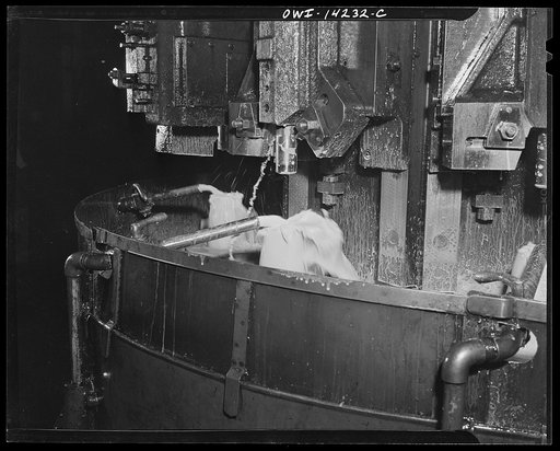 Detroit, Michigan. Steps in the manufacture of casings for 105 mm. shells in the Budd wheel plant. Threading the nose in the finishing machine. Lubricating fluid pouring over shell. The cutter is removed from the interior of the shell