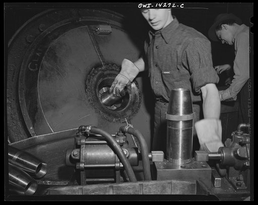 Detroit, Michigan. Steps in the maufacture of casings for 105 mm. shells in the Budd wheel plant. Applying gilding metal band to exterior of shell. Band shown in the upper part of shell will be dropped to surface of block and squeezed. It is then transfered to the machine shaped like an iris diaphra