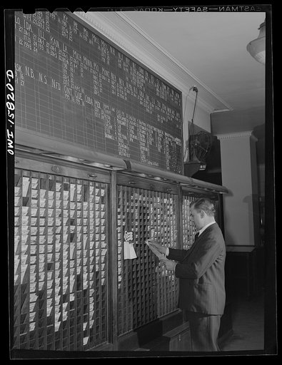 Chicago, Illinois. In the ticket selling department at Union Station. Ticket seller is selecting a ticket. On the blackboard above is a reference table volumes in which detailed information on rates and schedules may be found
