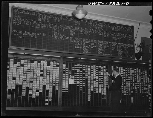 Chicago, Illinois. In the ticket selling department at Union Station. Ticket seller is selecting a ticket. On the blackboard above is a reference table volumes in which detailed information on rates and schedules may be found