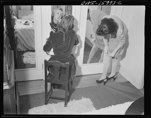 Detroit, Michigan. Girl putting on lipstick and another girl straightening seams in her stocking