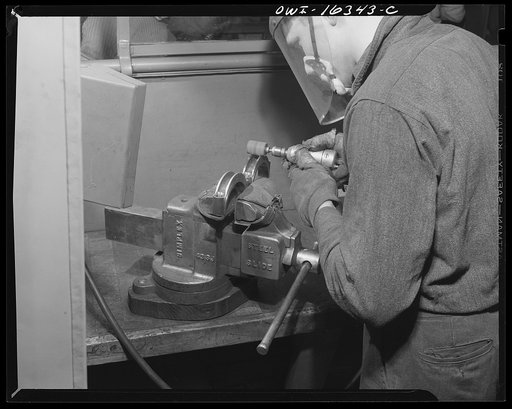Detroit, Michigan. An operation at the Cadillac motor car division of General Motors Corporation (?) with a jig holding two parts in a vise. A worker suggested the design for a jig to hold six of these parts at once, and so cut down handling time