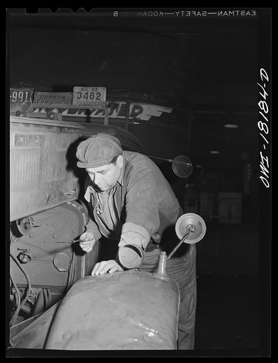 New York, New York. Associated Transport Company trucking terminal on Twenty-third Street. Local delivery driver checking the oil supply on a truck before taking it out