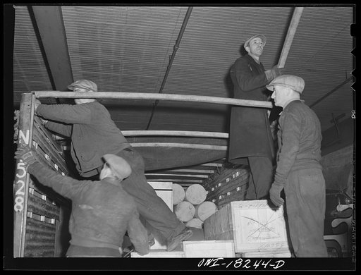 New York, New York. Associated Transport Company trucking terminal on Twenty-third Street. Rolling back canvas top of a local delivery truck