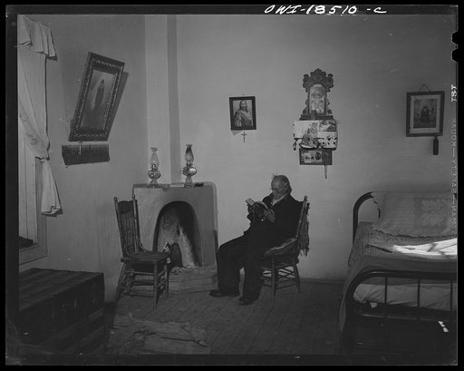 Untitled photo, possibly related to: Trampas, Taos County, New Mexico. Grandfather Romero, the oldest man in the town, is ninety-nine years old (seated in room, reading)