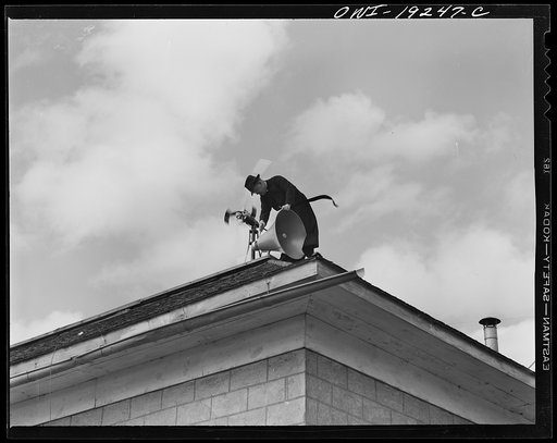 Questa, New Mexico. Father Smith adjusting his loudspeakers on top of the Questa parish house, where he daily broadcasts to the people