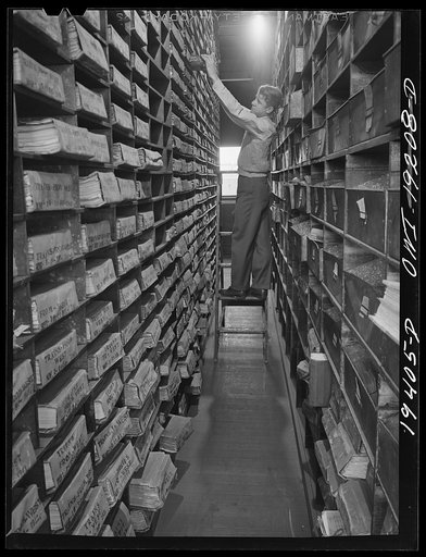 Untitled photo, possibly related to: Kansas City, Missouri. E. A. Schenck, teletype operator, looking up one of the files in the record room of the freight depot