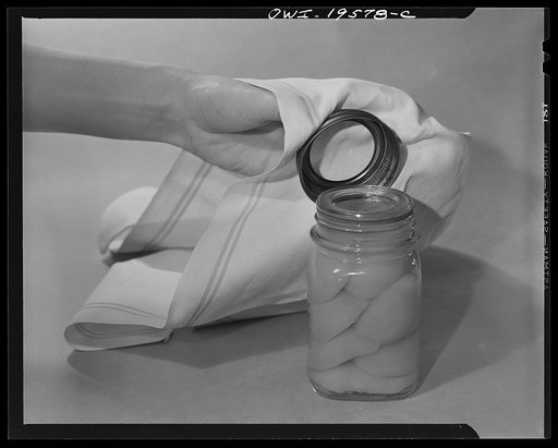 Steel-saving glass-top jars recommended by the War Production Board, Containers Division, for home canning of the Victory garden fruits and vegetables in 1943. Second step is to place the lid directly on top of the ring on the jar mouth which must be smooth, even and clean. To make a snug seal, lid 