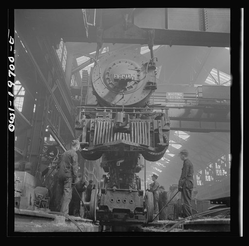 Untitled photo, possibly related to: Topeka, Kansas. Lifting an engine with the eighty-ton cranes at the Atchison, Topeka, and Santa Fe Railroad locomotive shops. This locomotive will be carried to another part of the shop to be wheeled