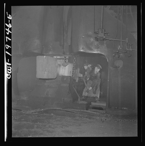 Untitled photo, possibly related to: Topeka, Kansas. Workmen manipulating a hot forging which is being hammered under a steam hammer in the blacksmith shop of the Atchison, Topeka and Santa Fe Railroad