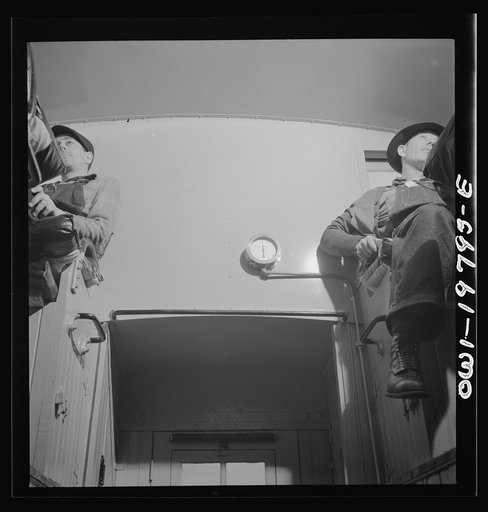 Conductor (right) and brakeman, in their places in the cupola of the caboose on the Atchison, Topeka, and Santa Fe Railroad between Argentine and Emporia, Kansas. On the wall between them is the air gauge showing the amount of air brake pressure in the train