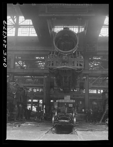 Albuquerque, New Mexico. Wheeling an engine in the Atchison, Topeka and Santa Fe Railroad locomotive shops. The engine has been raised so high to clear the locomotive on the floor as it was carried from another part of the shop