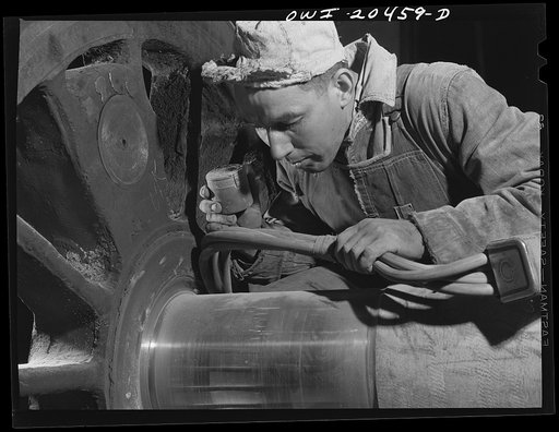 Albuquerque, New Mexico. Magnaflux inspector A.J. Fry at work on an engine wheel axle in the Atchison, Topeka and Santa Fe Railroad shop. The cable in his hand magnetizes the axle as he spreads steel dust over an area. He then cuts the current off and carefully blows the dust away. The steel particl