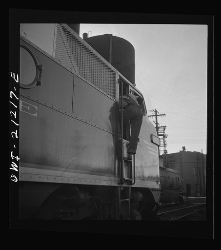 Untitled photo, possibly related to: Winslow, Arizona. An engineer climbing into the cab of a diesel freight engine in the Atchison, Topeka and Santa Fe Railroad yard