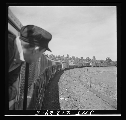 Williams, Arizona. A fireman watching a diesel freight train as it goes around a curve in the mountains on the Atchison, Topeka, and Santa Fe Railroad between Winslow and Seligman, Arizona