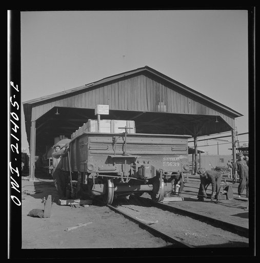 Untitled photo, possibly related to: Needles, California. Workmen jacking up a car at the rip tracks in the Atchison, Topeka, and Santa Fe Railroad yard