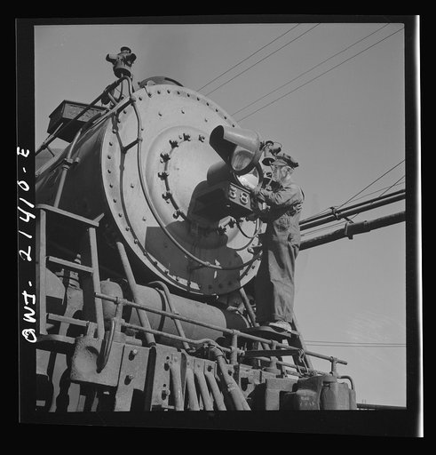 Needles, California. Electrician B. Fitzgerald cleaning the headlight of a locomotive at the Atchison, Topeka, and Santa Fe Railroad. All engines operating west of Needles are equipped with hooded headlights in accordance with the blackout regulations