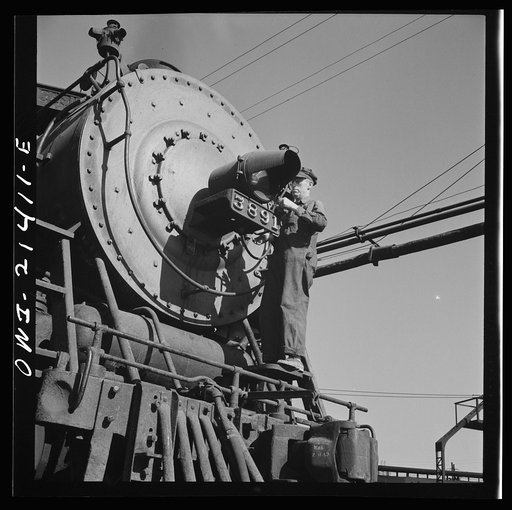 Untitled photo, possibly related to: Needles, California. Electrician B. Fitzgerald cleaning the headlight of a locomotive at the Atchison, Topeka, and Santa Fe Railroad. All engines operating west of Needles are equipped with hooded headlights in accordance with the blackout regulations