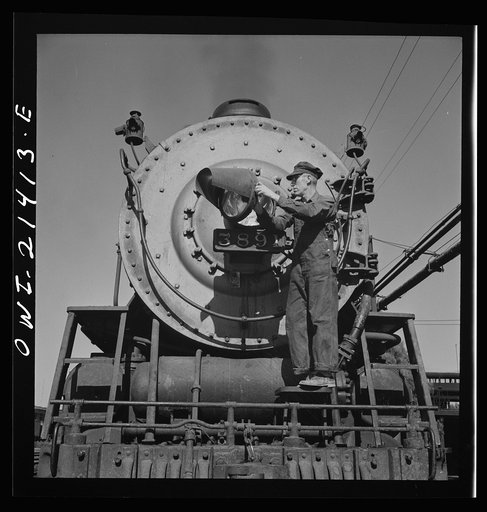 Untitled photo, possibly related to: Needles, California. Electrician B. Fitzgerald cleaning the headlight of a locomotive at the Atchison, Topeka, and Santa Fe Railroad. All engines operating west of Needles are equipped with hooded headlights in accordance with the blackout regulations
