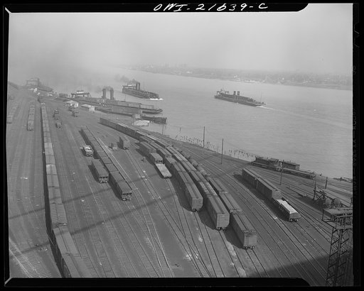 Detroit, Michigan (?). A railroad train yard in the Detroit area, showing freight boats in the background