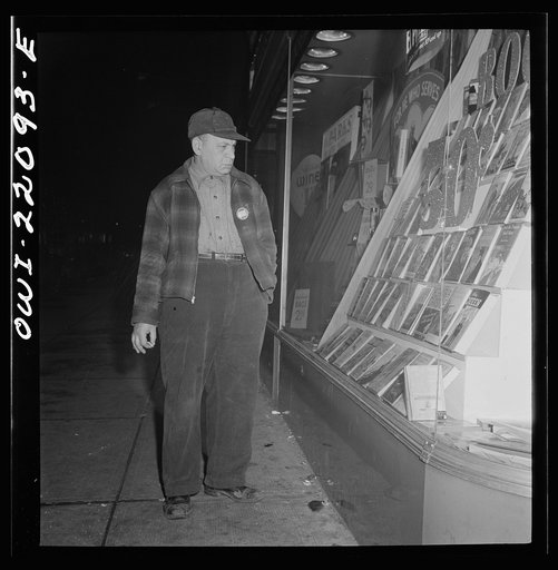 Baltimore, Maryland. Night shift worker waiting for the car which he shares in the "share the ride" program, looking at a drugstore book display