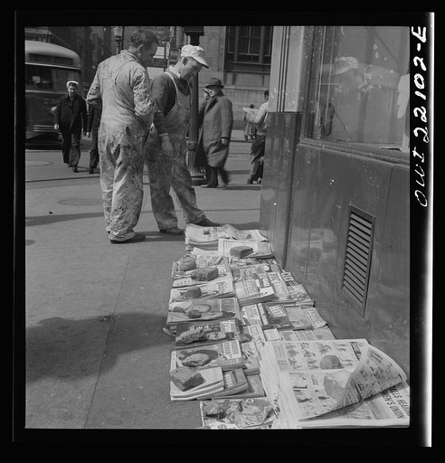 Baltimore, Maryland. Workers reading the newsstand papers while waiting for a trolley after work