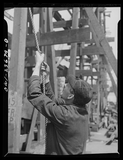 Bethlehem-Fairfield shipyards, Baltimore, Maryland. Pipe-fitter hoisting pipe with a rope and pulley