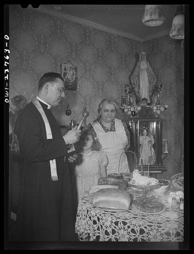 Buffalo, New York. Priest blessing the food-laden table on the Saturday before Easter at a home in the Polish community. Some bring their food in baskets to the church for blessing while others are visited by the priest. For Poles, Easter is a day of church going, visiting and feasting. This housewi