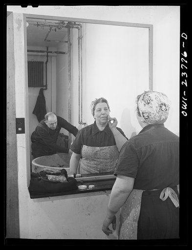 Untitled photo, possibly related to: Buffalo, New York. Italian-American woman, grinder and hooker at the New York Car Wheel Company, powdering her nose. This concern has only recently hired women, and the women's locker room is still unfinished. A plumber can be seen in the background installing a 