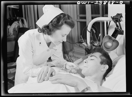 Encased in a body and leg cast, this soldier must have constant care. Here, Army nurse Frances Bullock helps him to a drink of fruit juice
