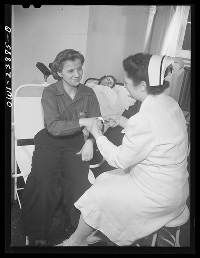 Buffalo, New York. A nurse in the first aid room at the Ross Heater plant bandaging a slight finger injury. Another woman worker rests in the background