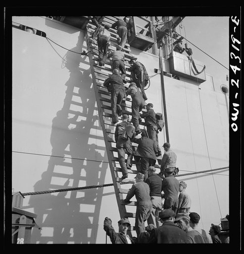 Bethlehem-Fairfield shipyards, Baltimore, Maryland. Workers on a ladder at the outfitting pier