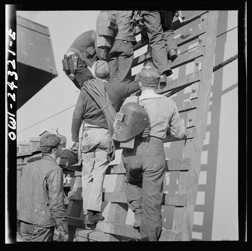 Bethlehem-Fairfield shipyards, Baltimore, Maryland. Workers on a ladder at the outfitting pier