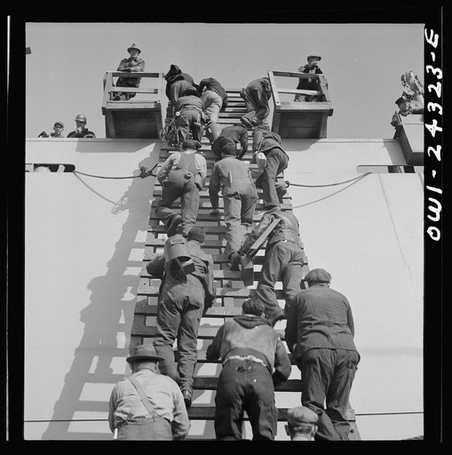Bethlehem-Fairfield shipyards, Baltimore, Maryland. Workers on a ladder at the outfitting pier