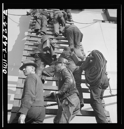 Bethlehem-Fairfield shipyards, Baltimore, Maryland. Workers on a ladder at the outfitting pier