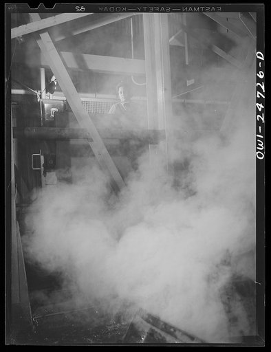 Buffalo, New York. Symongton-Gould, makers of tank, ship and railroad parts. Woman operating a charging machine. She works the machine by hand controls behind a partition, and has just dipped red hot metal into water, causing steam