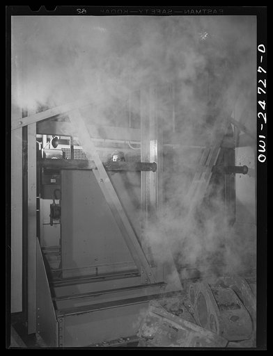 Buffalo, New York. Symongton-Gould, makers of tank, ship and railroad parts. Woman operating a charging machine. She works the machine by hand controls behind a partition, and has just dipped red hot metal into water, causing steam