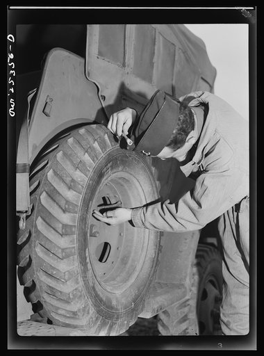 Holabird ordnance depot, Baltimore, Maryland. Jeep driver testing a tire valve for leakage by the old "spit of finger" method