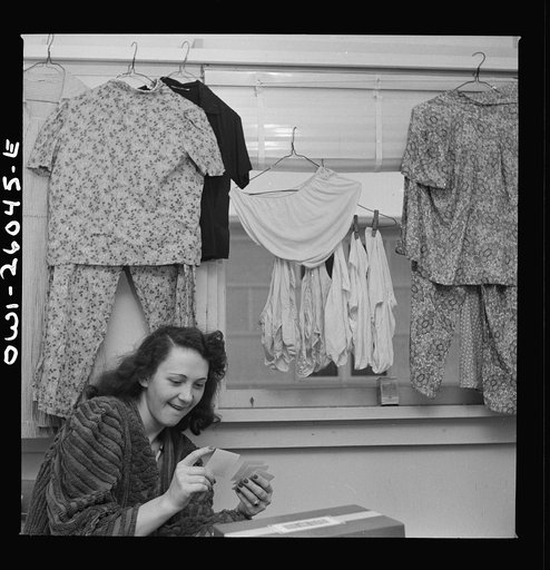 Arlington, Virginia. A girl looking at snapshots in her room at Idaho Hall, Arlington Farms, a residence for women who work in the U.S. government for the duration of the war. A typical room scene since there is a shortage of space in the laundries and authorities say that hanging the laundry outsid
