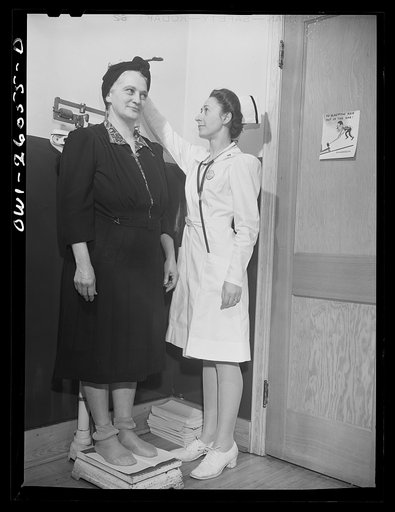 Buffalo, New York. After being interviewed as to past history and work qualifications, Mabel Goodwin has a physical examination at the Bell Aircraft plant. A nurse records her height and weight. She is forty-five, worked in a factory in the last war, and has since been a housewife and has two childr