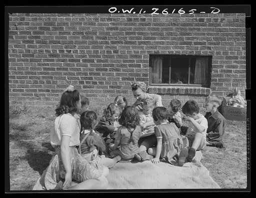 Washington, D.C. A day nursery for pre-school children of mothers engaged in war work, operated under the supervision of the District of Columbia Health Department by Mrs. Leroy Bonbrest at her home at 1144 Branch Avenue, S.E. Mrs. Bonbrest and the children out in the yard looking at a picture book