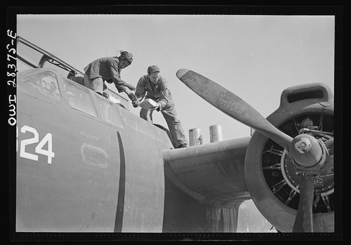 An American plane mechanic assisted by an Iranian boy working on a light bomber before delivery to Russia. Somewhere in Iran